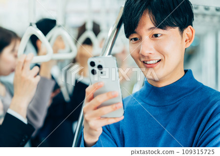 一名年輕人在火車上看智慧型手機。攝影由京王電鐵株式會社提供。 109315725