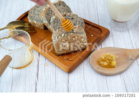 Breakfast set A man's hand is pouring honey onto bread with milk. Breakfast set A man's hand is pouring honey onto bread with milk. 109317281