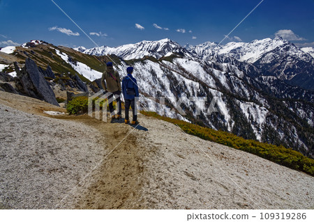 Climbers walking along the Tsubakudake ridgeline in the Northern Alps and a view of Mt. Yarigatake covered in remaining snow 109319286