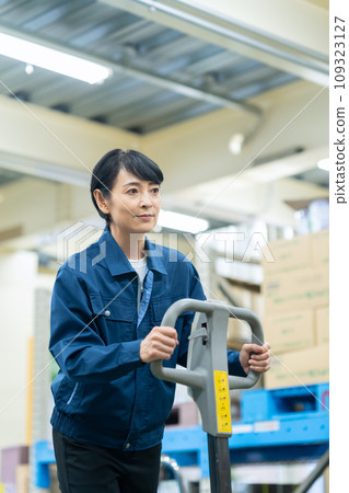 A middle-aged female worker using a hand lift to transport cargo in a warehouse A middle-aged female worker using a hand lift to transport cargo in a warehouse 109323127