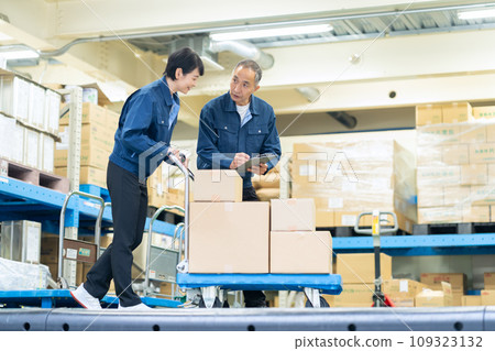Senior male and female workers using hand lifts to carry cargo in a warehouse Senior male and female workers using hand lifts to carry cargo in a warehouse 109323132