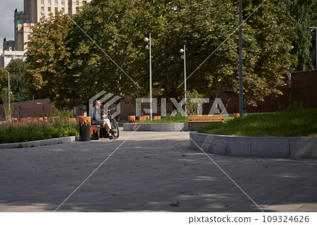 Man in a bicycle helmet sits on a bench and looks at his phone, resting while cycling in the city Man in a bicycle helmet sits on a bench and looks at his phone, resting while cycling in the city 109324626