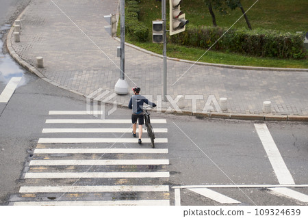 Man crosses the road at a pedestrian crossing and carries a bicycle next to him. View from above. 109324639