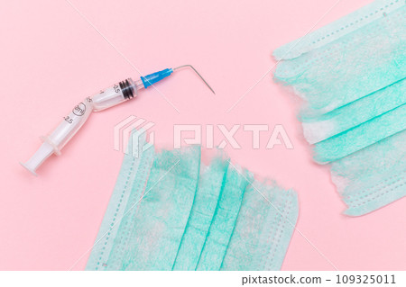 Broken Medical Syringe and Torn Medical Face Mask on the Pink Background Broken Medical Syringe and Torn Medical Face Mask on the Pink Background 109325011