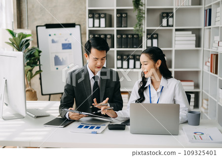 Two business workers talking on the smartphone and using laptop at the office. Two business workers talking on the smartphone and using laptop at the office. 109325401