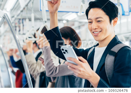 A man in casual office clothes on a commuter train. Photography provided by Keio Electric Railway Co., Ltd. 109326476