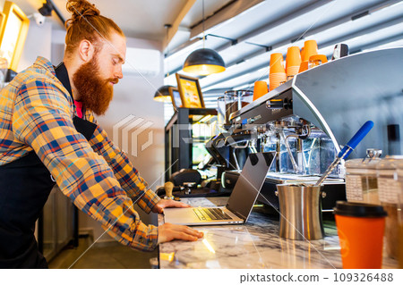 Professional barista young redhaired ginger bearded man in black apron working in coffee shop 109326488