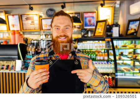 Professional barista young redhaired ginger bearded man in black apron working in coffee shop 109326501