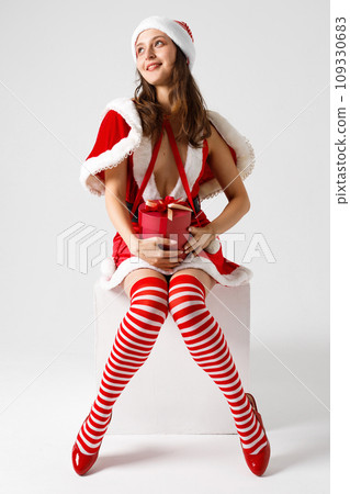 Beautiful woman wearing santa claus clothes sitting with gift. Beautiful woman wearing santa claus clothes sitting with gift. 109330683