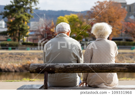 Friendly elderly couple sitting on a bench by the river Friendly elderly couple sitting on a bench by the river 109331968