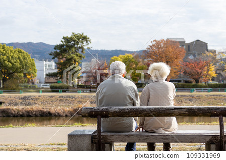 Friendly elderly couple sitting on a bench by the river Friendly elderly couple sitting on a bench by the river 109331969