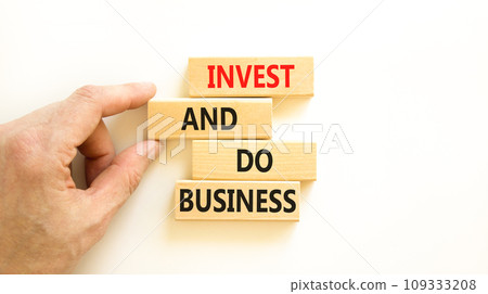 Invest and do business symbol. Concept word Invest and do business on beautiful wooden block. Beautiful white table white background. Businessman hand. Invest and do business concept. Copy space. Invest and do business symbol. Concept word Invest and do business on beautiful wooden block. Beautiful white table white background. Businessman hand. Invest and do business concept. Copy space. 109333208