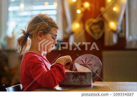 Happy little girl eating gingerbread Christmas cookies in domestic kitchen decorated with lights. Cute school child with biscuit jar. 109334887