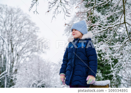Portrait of little girl in winter. Happy cute school child with warm clothes, knitted blue hat. Cold season, walking with children. Portrait of little girl in winter. Happy cute school child with warm clothes, knitted blue hat. Cold season, walking with children. 109334891