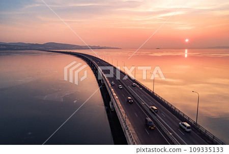 Aerial drone view of low-water bridge across the bay with moving car during the sunset. Active movement of transport cars vehicles in different directions. 109335133