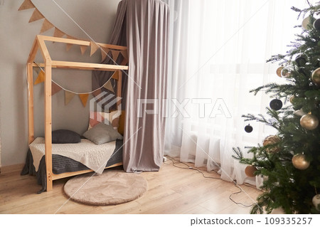In the children's bed in the form of a house, there is a decorated Christmas tree with Christmas balls. The concept of waiting for the New Year. High quality photo In the children's bed in the form of a house, there is a decorated Christmas tree with Christmas balls. The concept of waiting for the New Year. High quality photo 109335257