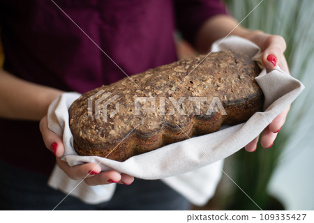 Baker man holding rustic organic loaf of bread and wheat in hands - rural bakery. Natural light, moody still life. 109335427