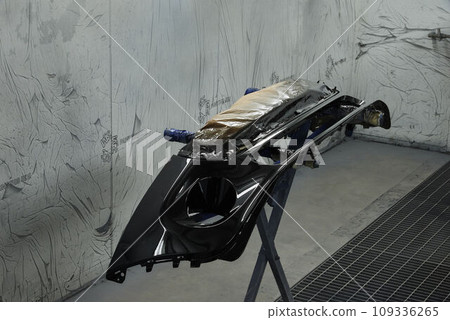 The photograph captures the scene of an automotive workshop, showcasing the process of painting various car parts. Different components of the vehicle car bonnet, bumpers, smaller details. The photograph captures the scene of an automotive workshop, showcasing the process of painting various car parts. Different components of the vehicle car bonnet, bumpers, smaller details. 109336265
