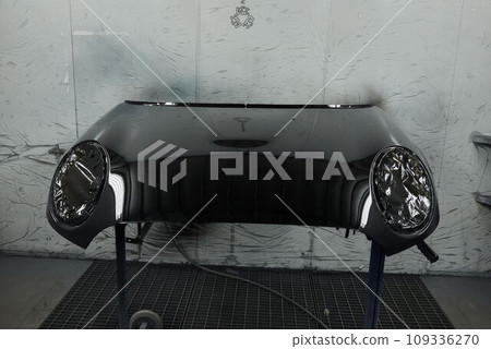 The photograph captures the scene of an automotive workshop, showcasing the process of painting various car parts. Different components of the vehicle car bonnet, bumpers, smaller details. 109336270
