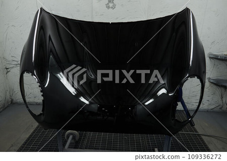 The photograph captures the scene of an automotive workshop, showcasing the process of painting various car parts. Different components of the vehicle car bonnet, bumpers, smaller details. 109336272