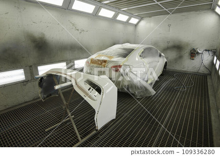 The photograph captures the scene of an automotive workshop, showcasing the process of painting various car parts. Different components of the vehicle car bonnet, bumpers, smaller details. The photograph captures the scene of an automotive workshop, showcasing the process of painting various car parts. Different components of the vehicle car bonnet, bumpers, smaller details. 109336280