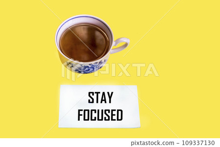 STAY FOCUS phrase on notepad and yellow background with cup of tea. STAY FOCUS phrase on notepad and yellow background with cup of tea. 109337130