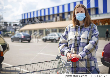 Woman wears medical mask while leaning on shopping cart outside of grocery store Woman wears medical mask while leaning on shopping cart outside of grocery store 109337176