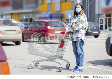 Woman wears medical mask while leaning on shopping cart outside of grocery store Woman wears medical mask while leaning on shopping cart outside of grocery store 109337177