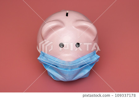 Concept of economic crisis. Piggy bank with protective mask on pink background Concept of economic crisis. Piggy bank with protective mask on pink background 109337178