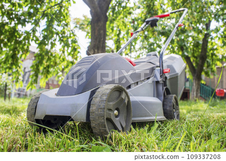 Lawn mower on a lawn on a background of trees. Outdoor shot of lawnmower Lawn mower on a lawn on a background of trees. Outdoor shot of lawnmower 109337208