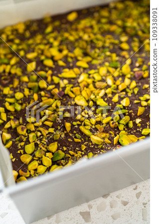 Removing chocolate pistachio fudge from a square cheesecake pan lined with parchment. 109338091