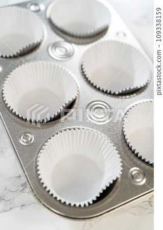 Cupcake foil liners are being meticulously filled with both chocolate and vanilla batter, setting the stage for the baking of deliciously diverse birthday cupcakes. 109338159