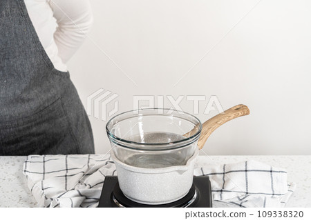 Melting chocolate chips and other ingredients in a glass mixing bowl over boiling water to prepare plain fudge. 109338320