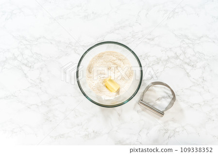 Flat lay. Mixing dry ingredients with a hand whisk in a glass mixing bowl to bake no-yeast cinnamon roll cupcakes. Flat lay. Mixing dry ingredients with a hand whisk in a glass mixing bowl to bake no-yeast cinnamon roll cupcakes. 109338352