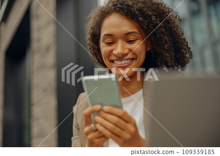 Smiling businesswoman working on laptop and use mobile phone while sitting in cafe terrace Smiling businesswoman working on laptop and use mobile phone while sitting in cafe terrace 109339185