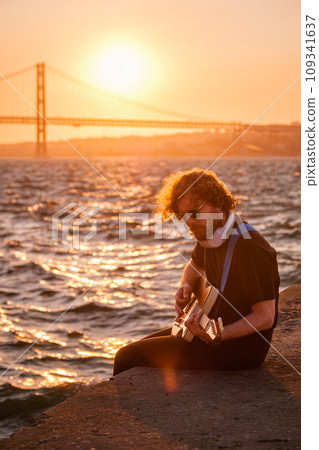 Hipster street musician in black playing electric guitar in street outdoors on sunset 109341637