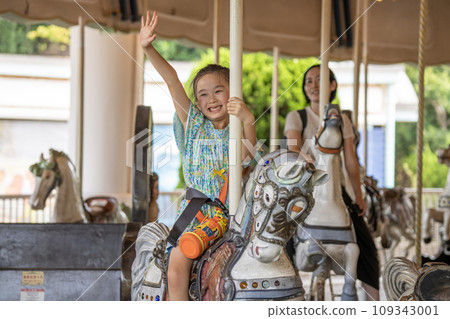 A girl and her mother having fun on a merry-go-round 109343001