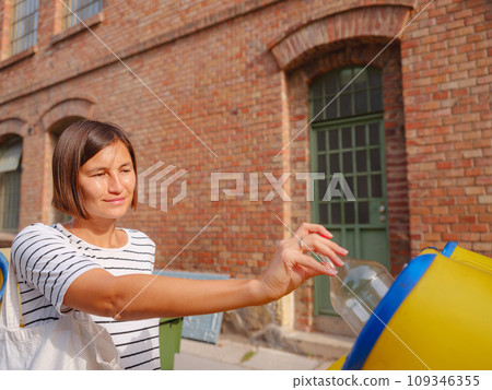 woman throwing plastic bottle Recycling bin stand on european street. Waste separation rubbish before drop to garbage bin to save world, environment care. Pollution trash recycling management concept 109346355