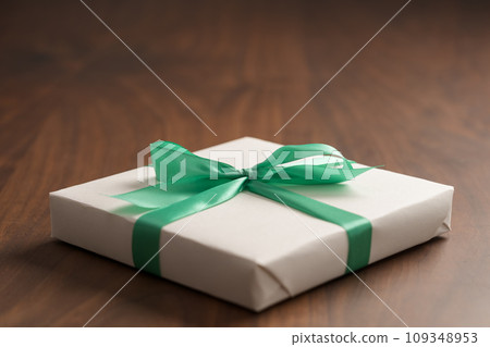 White paper gift box with green ribbon on walnut wood table with copy space 109348953