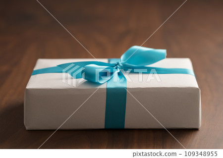White paper gift box with blue ribbon on walnut wood table with copy space White paper gift box with blue ribbon on walnut wood table with copy space 109348955