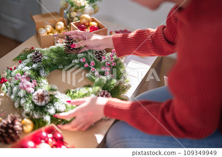 Young asian woman in sweater with happiness decorating pine cone and red berries on christmas wreath while preparing ornaments to celebrate for christmas festive holiday and winter seasons in house Young asian woman in sweater with happiness decorating pine cone and red berries on christmas wreath while preparing ornaments to celebrate for christmas festive holiday and winter seasons in house 109349949