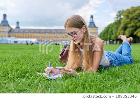Young student girl lying on grass, educational building background 109353346