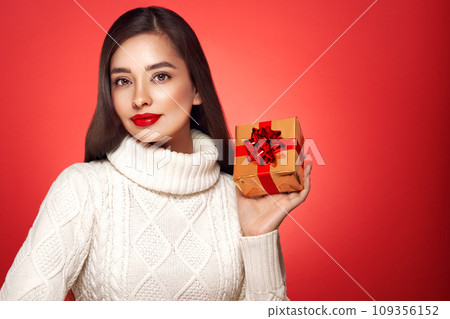 Beautiful woman in a white knitted sweater with gift box Beautiful woman in a white knitted sweater with gift box 109356152
