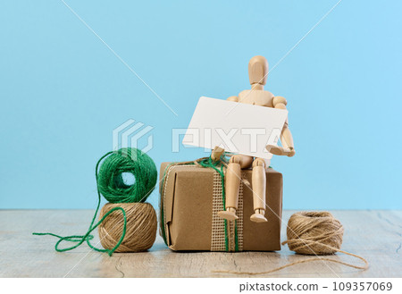 Wooden mannequin holding a white paper business card and gifts wrapped in brown craft paper on a blue background Wooden mannequin holding a white paper business card and gifts wrapped in brown craft paper on a blue background 109357069