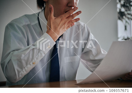 一名年輕的男性上班族看著文件時顯得很驚訝。 一名年輕的男性上班族看著文件時顯得很驚訝。 109357671