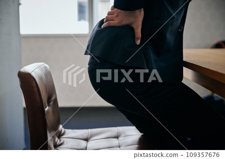 A young male office worker has a pain in his lower back and holds it down with his hand. 109357676
