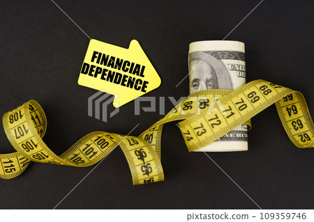 On a black surface there are dollars wrapped in measuring tape and stickers with the inscription - financial dependence 109359746