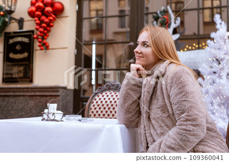 Attractive young woman sits at a outdoor cafe during the Christmas holidays. Winter walk through the city. 109360041