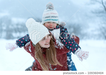 Young mother or older sister wrils small child on her back. Babysitter and child fool around in the winter. Young mother or older sister wrils small child on her back. Babysitter and child fool around in the winter. 109360484