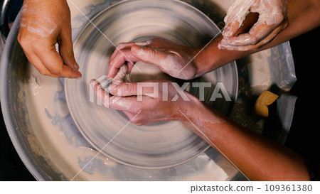Close-up of a female potter's hands moulding and shaping a stunning piece of white clay pottery. The hands of a mentor helping a student. Open lesson. The concept of manual labour, art and craft. 109361380